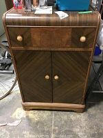 Front view of wooden liquor cabinet showing drawer and double doors with round knobs, woodgrain veneer finish.