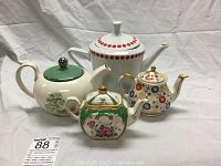 Photo showing four fine china teapots in varying sizes and floral designs including red dotted lid, gold-trimmed floral teapot, green lid floral motif, and leaf design teapot