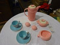 Complete set on round table showing all items: pink coffee pot, sugar bowl with lid, cream bowl, salt and pepper shakers, and 2 blue cups with saucers