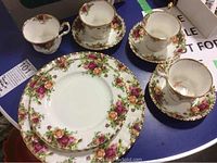 Five Royal Albert fine bone china cups, matching saucers, and two dinner plates with floral design and gold rim on blue table surface.
