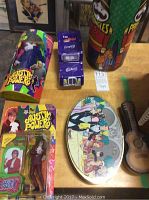 Photo showing Austin Powers action figure in packaging, metal Cadbury truck, Pringles tin, and two collectible tins including guitar-shaped and oval-shaped tins.