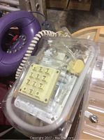 Close-up of clear plastic push-button telephone with visible inner components and yellow keypad dial.