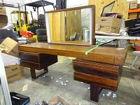 Wide angle front view of the wooden vanity with mirror and drawers, showing overall shape and condition.
