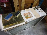 Overall view of Seagram's 83 Centennial portfolio with gold embossed cover, loose painting prints, and some harmonicas on top.