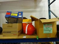 View of assorted boxes on shelf including the red spherical container holding plastic plates and blue binoculars case.