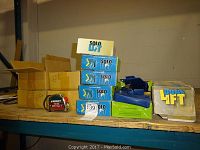 Photo showing four blue boxed Solo Lift single handed box lifting tools and a Signet measuring tape on a shelf.