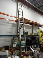 Full length of aluminum extension ladder extended against warehouse shelving with assorted items around