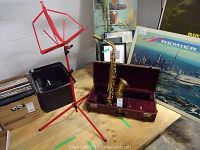Alto saxophone seated in open brown case with red plush lining on wooden table.