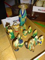 Group photo of all 12 Asian style ceramic figurines in a cardboard tray on wooden surface.