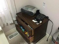 Photo of wooden set of drawers with Sony stereo on top and Olympus camera beside it.