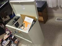 Metal cabinet with top compartment open displaying boxed Creative Live Cam and office supplies inside.