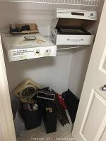 Photo showing shelf with boxed VIVI laptop tray, white box containing a digital photo frame, and assorted smaller black boxes and electronics. Below shelf are a beige triangular analog wall clock, black rectangular alarm clock, briefcase, and bags with other items.