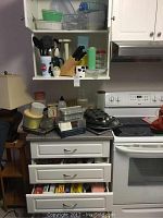 Photo of kitchen counter and open drawers showing muffin tins, aluminum pans, measuring cups, plastic containers, knives in bamboo block, and some utensils in cups.