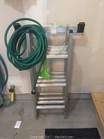 Folded ladder leaning against wall with green hose draped over top rung