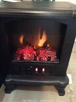 Front view of the black electric fireplace stove with glowing ember and flame effect, showing dual control switches on front panel.