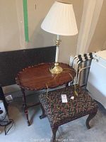 Overview of pie crust wooden table, floral upholstered ottoman, and brass table lamp