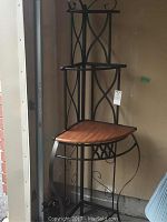 Full view of the corner shelf showing three wood shelves and black metal frame with decorative scroll and criss-cross design.