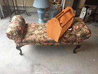Floral upholstered bench with wooden magazine stand placed on top of it, showing the bench's armrests, seat, and legs.
