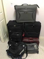 Photo of entire lot showing all luggage pieces stacked together including large gray suitcase on top, two black suitcases, maroon hard case, and two duffel bags at bottom.