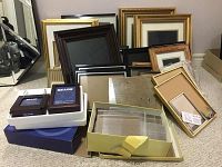 Various sized picture frames including large gold and brown wood frames, small black and silver frames, and boxed Sears branded frames arranged on carpet.