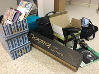 Lot showing Giottos VT 806 3-way tripod box in front, JVC Handycam box and camera bags behind, striped blue and white photo storage boxes to left, and other items on carpeted floor.