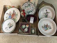 Wide view showing multiple Asian china plates with cultural designs including dragons and classical figures alongside a ceramic bottle and decorative eggs.