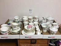 Three boxed trays with assorted fine bone china items including cups, saucers, bowls, side plates. Floral designs and gold rims visible.