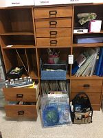 Front view of wooden cabinet with open drawers and shelves containing visible scrapbooking items like papers, folders, tools, and containers.