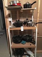 Shelf with cookware items including black Plasma Innovation pots and pans with glass lids, small stainless steel Star Basix pot with handle, a cooking tray and red pot