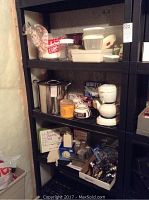 Black shelving unit holding kitchen items such as stock pot, teapots, water filter, and containers.