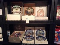 Collector decorative plates arranged on shelving; top shelf has 3 plates, bottom shelf has 4 plates and boxed collector spoons