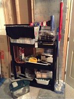 Full view of black shelving unit with multiple plastic storage bins containing tools and hardware, plus a red umbrella or flag propped alongside.