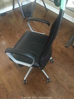 Side view showing black mesh back, padded seat, curved armrest, and white base of office chair.