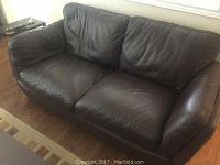 Front angle view of the brown leather sofa showing seating cushions and armrests.