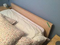 View of queen bed showing light wood headboard and part of bed linens and pillows