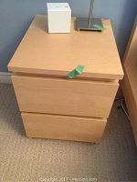 Front view of light wood IKEA nightstand with two drawers, slight wear marked by green tape on the top edge.