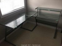 Full view of L-shaped glass desk showing main and side glass surfaces and metal frame