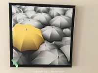 Front view of the framed fabric artwork showing the distinctive yellow umbrella among grey umbrellas.