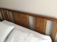 Front view of wooden king size headboard attached to a bed, showing natural wood finish and design details.