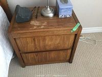 Front and side view of one wooden night stand showing scratches and wear on top surface and sides.