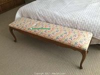 Long upholstered bench placed in front of a bed, showing full side profile with floral patterned fabric and wooden legs.