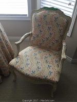 Front view of one upholstered armchair with carved wood frame and floral fabric upholstery.