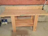 Front view of the solid spruce workbench on concrete floor in basement with natural wood finish and measuring tape on top.