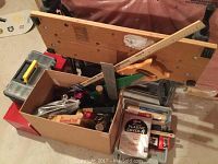 View of workbench behind a box containing hand tools and two plastic empty toolboxes stacked.