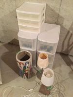 Overall photo showing two white plastic multi-drawer storage bins, a small 4-drawer plastic bin, two table lamps with shades, and ceramic umbrella holder.