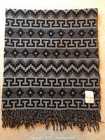 Full view of folded rectangular black and grey alpaca blanket with geometric patterns and fringed edges.