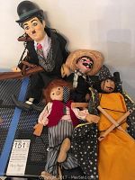 Group photo of four marionette puppets arranged on a blue and white woven mat, displaying various costumes and painted faces.