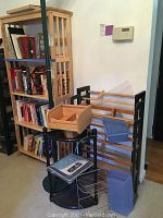 Green metal floor lamp with glass shelf and various wooden bookcase and CD racks containing books and storage bins