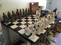 Chess board and full set of black and white ceramic chess pieces arranged on table.
