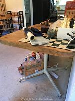 View of the full laminated kitchen table with metal frame and wheels showing wear and scratches on the tabletop, and the base structure including caster wheels.